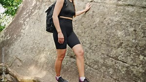 Active female hiker climbs steep rocky terrain in mountain gorge. Backpack, fitness cap, and sports outfit, she navigates roots and boulders, embracing nature challenge. Slow motion.