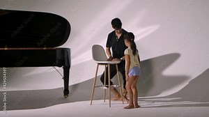 Personal ballet lesson for little girl. Professional teacher teaches child elements of dance and corrects positioning legs and stretching. Diligent ballet student trains on white studio background.