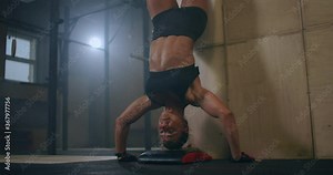 a strong woman performs vertical push-ups standing on her head in the gym. perform push-UPS upside down. push-UPS against the wall upside down