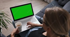 woman sitting on a couch at home and scrolling laptop computer. blank green screen copy space