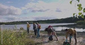 A heartwarming scene as a diverse group of friends from different backgrounds come together for an environmental cleanup on a tranquil forest lake beach, promoting unity and conservation Stock Video