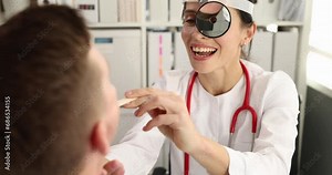 Doctor with frontal reflector on forehead examining throat of male patient with spatula 4k movie slow motion. Diagnosis and treatment of nasopharyngeal diseases concept