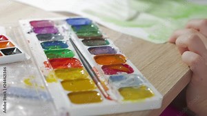 Teenage girl at home is engaged in creativity, draws watercolor at a table in room. Child drawing top view. Artwork workplace with creative accessories.