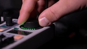 Close-up image of hand adjusting mixer knob for volume control during live studio performance. Mixer features multiple knobs and buttons for precise audio mix adjustments.