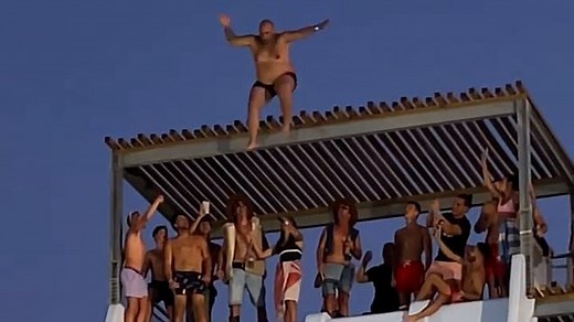 Insane moment man jumps off roof slide and belly flops into water