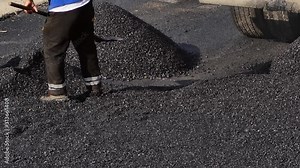 Pouring asphalt worker uses a shovel to level and smooth the hot asphalt on floor in the road construction site. Seal coating is a street maintenance technique which preserves the condition of street