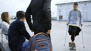 Skill young man with one leg on crutches training and three of his friends supporting him. Guys shaking hands, hugging and smiling. Disabled person rides on a skateboard. Motivation, active lifestyle Stock Video