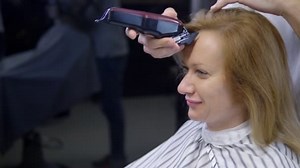 Frau rasiert sich den Kopf kahl. ein Friseur rasiert eine Frau lange Haare mit einem Haarschneider.