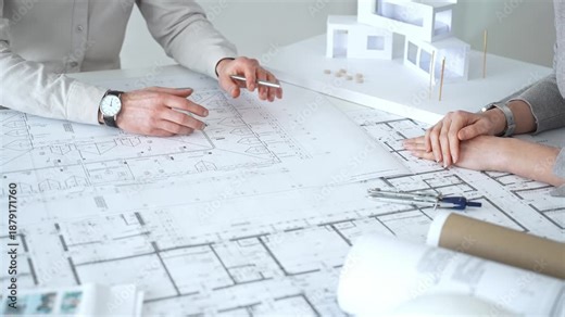 Architects discussing architectural blueprints and a building model on a white desk, planning a new construction project and developing innovative design solutions collaboratively, close up