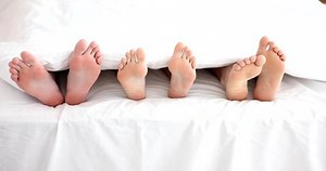 Legs of woman with two men in bed