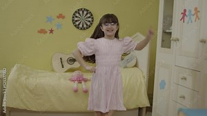 Portrait of happy little girl dancing, having fun alone in her room in their house.Little girl is having a party alone.Funny girl is dancing, jumping, singing.