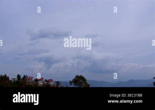 Time-lapse view of Mukteshwar, Uttarakhand, India, capturing dramatic cloud formations sweeping across a vast sky above red-roofed hillside villas, misty mountain layers fading into distance below Stock Video Footage - Alamy