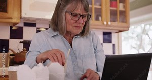 Retired senior woman having lunch and using laptop computer in her kitchen, Old lady eating Chinese food while using portable computer in kitchen setting, 4k Stock Video