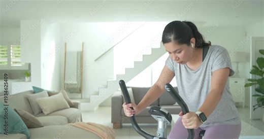 Woman gripping handlebars, starting pedaling on stationary bike at home, checking console