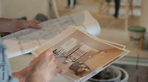 Close-up shooting of drawing Builders make repairs in apartment in new house, check parameters. Close-up Shot man holds large white sheet, photo with architectural design of building, furniture
