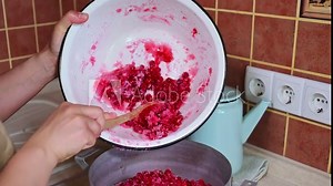 Close-up hands of a chef pastry putting grated red currant berries with sugar from an enamel bowl into a metal pan for making jam