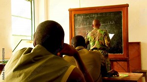 Inside a military class room, one man stands and writes on the blackboard while cadets listen intently at their desks