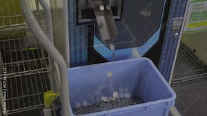 This zooming out video shows a coin vending machine dropping coins into a bucket in slow motion.
