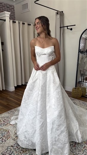 Meet Sierra, named after our stunning stylist! ✨ This dress features a classic strapless sweetheart neckline with a fitted, structured basque bodice that flows into a dramatic full skirt. The entire gown is covered in beautiful textured floral jacquard fabric with roses and blooms that create incredible depth and dimension. The voluminous A-line silhouette with a sweeping train is pure fairytale magic—absolutely twirl-worthy! #elopebride #basque #weddingdressshopping #bridalshopping #lakeland #b