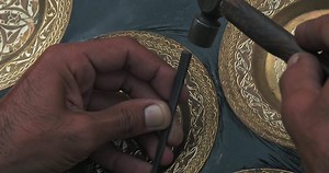 A master embosser creates a pattern on a copper plate using ancient technologies.