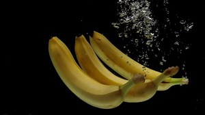 Slow motion three bananas falling into transparent water on black background. Fresh fruits splashing in aquarium. Healthy food, diet, air bubbles