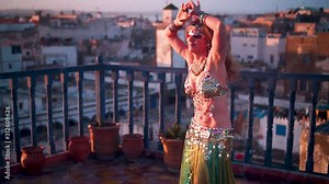 Beautiful belly dancer doing hip thrusts at sunset performing on a rooftop in Morocco.