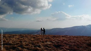 silhouette of the bride goes to the groom, the wedding couple runs up to each other, on top of the mountain, with landscapes of amazing nature. Blue sky and rocks, aerial view