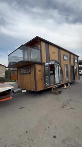 4.1M views · 113K reactions | This tiny house build by @tahtalandik has a modern, wood-paneled exterior with black metal accents. It features large circular windows, one of which opens onto a small balcony with glass railings. The structure sits on a trailer, indicating mobility, and has multiple windows along the side. #tinyhouse #tinyhome #tinyhomes #tinyhouseattractive | Archi Benes | Facebook