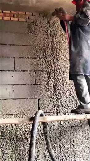Spraying wet cement onto a cinder block wall to create a textured finish