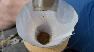 Man pours freshly ground coffee into a funnel with a paper filter for making aromatic coffee in an alternative way in nature close-up