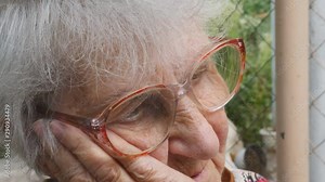 Portrait of grandmother with emotions and feelings. Old woman looking with sad expression outdoor. Grandma keeping hand at her face and sighing heavily. Close up Side view Slow motion