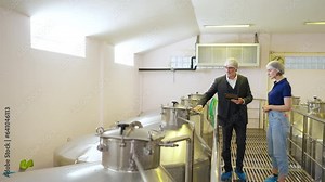 Professional man and woman winemaker working and inspecting wine quality in wine cellar with stainless steel barrel in wine factory. Winery manufacturing industry and winemaking fermentation process.