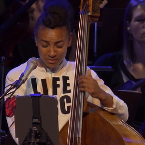 Watch the San Francisco Symphony and esperanza spalding perform Wayne Shorter’s “Gaia." "San Francisco Symphony’s Reopening Night Concert" premieres tonight at 9/8c on PBS. [VID: esperanza spalding playing upright bass and singing with the San Francisco Symphony.] Video transcript: [Vocalizing] Gaia's Shuttle Rocks our Spinning cradle [Vocalizing] Age in, age out Spinning life in circles [Vocalizing] Patterns of fruited empires And fall as entire Worlds bear the reaping Blooming, progress and wi