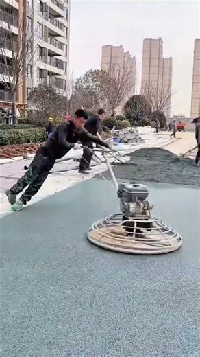 Smoothing green playground floor with power trowel and spreading synthetic turf materials outdoors