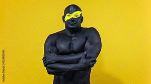 Man sports fan celebrates team victory or goal. Bodybuilder athlete with yellow color on face art and black body paint. Colorful portrait of the guy with bodyart. Slow motion.