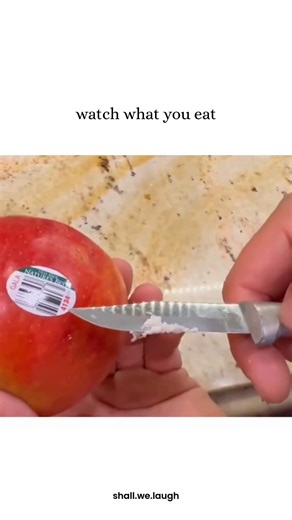 Shall we laugh? on Instagram: "The post shares a 37-second close-up video of a pair of hands holding a red Gala apple while using a knife to scrape a thick, white, waxy substance from the surface, captioned "watch what you eat" to serve as a stark warning about commercially grown produce. It generated 900K likes and 15.8M views within a week, instantly tapping into the highly viral health and food safety awareness niche, where content creators expose perceived dangers in grocery store products. 