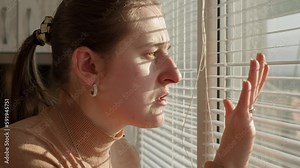 Young woman saw crime happening on street through window blinds. Crime witness, spying through window, peeking on street