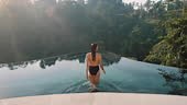 attractive woman walking into infinity pool enjoying luxury lifestyle...