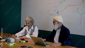 Couple of aged employees collaborating on idea for graphic design using netbook application and papers in coworking board room,Caucasian male and female discussing business while developing project