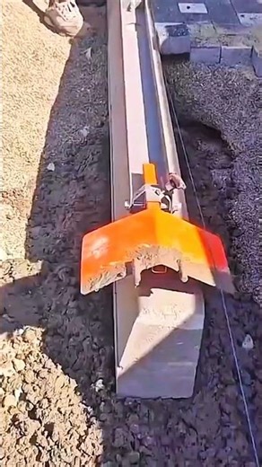 Orange blade grades soil—sneakered stride guides leveling tool past string line toward laid pavers.