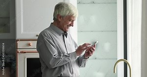 Senior man holds smartphone text message, share sms standing alone in cozy kitchen. Older generation and modern wireless tech, mobile app usage for comfort living, make products order at home concept