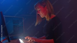 Girl Hacker tries to enter the system using codes to find out the security password. Her hideout place has dark atmosphere and blue neon light. Hacker girl is surrounded by displays and smoke.