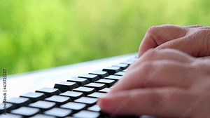 female hand with wrinkles close-up type text on a computer keyboard on a natural background, workplace outdoors, the concept of the daily routine of a freelancer, programmer, downshifter