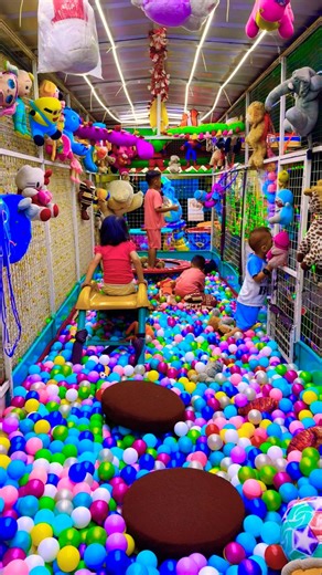The little brother in red goes down the yellow slide and the older brother jumps on the trampoline.
