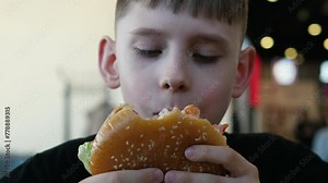 Tasty moments, Caucasian boy 10 years old enjoys a delicious cheeseburger in a cafe. fast food concept, schoolboy enjoying a burger in the cafeteria