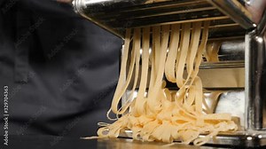 Traditional italian homemade pasta being made on hand machine for cutting dough. Slow motion food footage of Fresh spaghetti pasta coming out of pasta machine, close-up. Chef use pasta cutting machine