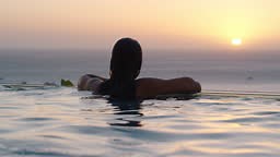 woman swimming in pool at luxury hotel spa with beautiful sunset view...