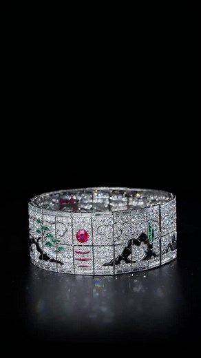 This extraordinary bracelet made in 1925 by Lacloche Frères is a rare example in the Jewellery History of the art of gemstone carving. Like a Japanese scroll, the Japanese-inspired design unfolds before our eyes, beginning with a realistic cherry blossom tree blooming in a Japanese garden with all the attributes of Japanese representations. The center of the bracelet depicts a temple overlooking a river on which floats a pagoda set with diamonds, rubies, and onyx, dominated by a rising sun set w