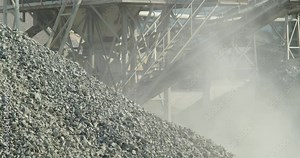 Bulldozer operator loading and transporting stones in scoop during the separation of building materials in stone crusher plant. Excavator at work in the quarry. Dust and smoke rising
