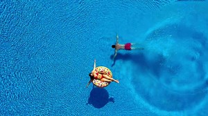 Aerial view of man dives into the the pool while girl is lying on a donut pool float